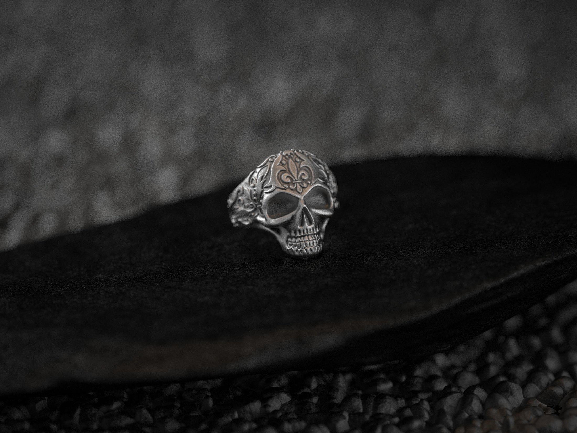 Angled view of ornate silver skull ring on textured pedestal.
