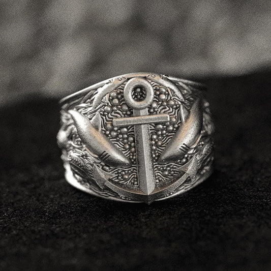 Close-up of sterling silver anchor and sharks signet ring on black stone.