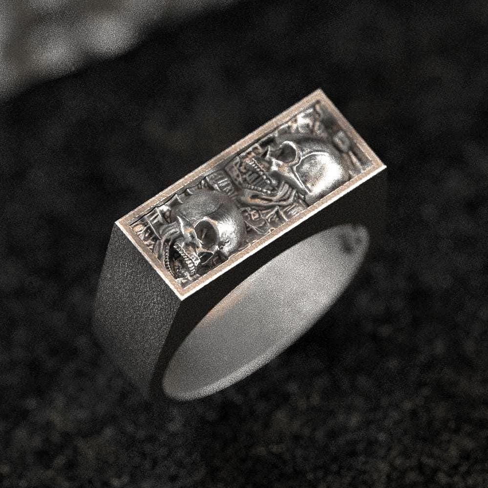 Three-quarter top-down view of the sterling silver bar signet ring showcasing two skull reliefs side by side on a rectangular face.