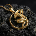 Load image into Gallery viewer, Gold plated alien xenomorph pendant showcased on volcanic rock as dark sci-fi horror statement jewelry