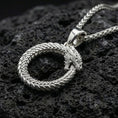 Load image into Gallery viewer, Polished silver ouroboros dragon serpent necklace displayed on volcanic stone background highlighting circular rebirth symbolism