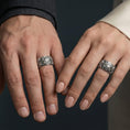 Load image into Gallery viewer, Oxidized sterling silver ornate cross band ring worn on a finger on a man and woman, lifestyle wear image showing bold sculpted depth and vintage-style contrast in natural light.