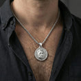 Load image into Gallery viewer, Polished silver Zeus pendant on chain worn on neck, natural lifestyle framing, Zeus face and Greek key border visible