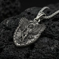 Load image into Gallery viewer, Oxidized Archangel Michael shield pendant on textured volcanic rock, macro close-up, detailed wings and sword relief, premium studio lighting