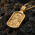 Load image into Gallery viewer, Gold plated Saint Roch dog tag pendant displayed on porous volcanic rock surface, close-up studio composition, detailed saint figure and dog relief