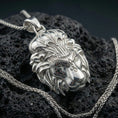 Load image into Gallery viewer, Polished silver lion head pendant on black volcanic stone, sharp facial contours and ornate forehead engraving, luxury product photo