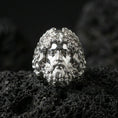 Load image into Gallery viewer, Polished silver Zeus head ring with flowing hair and beard sculpture, centered close-up jewelry shot on dark porous volcanic stone