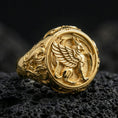 Load image into Gallery viewer, Gold plated griffon signet ring with high-relief mythical griffin motif and ornate border, premium studio macro on black volcanic rock surface