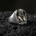 Load image into Gallery viewer, Detailed griffin guardian signet ring crafted in oxidized sterling silver, seated winged beast with lion body, macro product shot on textured volcanic rock background