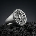 Load image into Gallery viewer, Detailed Chinese dragon signet ring crafted in oxidized sterling silver, coiled dragon with spread wings relief, macro product shot on textured volcanic rock background