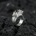 Load image into Gallery viewer, Polished silver twin dragons ring featuring paired dragon head design and engraved scale detailing, centered close-up on dark porous volcanic stone