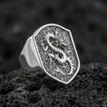 Load image into Gallery viewer, Polished silver Chinese dragon ring featuring sculpted dragon emblem on shield-shaped signet and hammered texture detail, centered close-up on dark volcanic stone