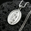 Load image into Gallery viewer, Polished silver Guadalupe medallion necklace on dark volcanic stone, crisp Marian figure detail and smooth oval bezel, premium close-up composition