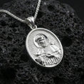 Load image into Gallery viewer, Polished silver St Francis oval pendant necklace on dark volcanic stone, crisp saint portrait engraving and smooth bezel edge, premium close-up