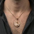 Load image into Gallery viewer, Rose gold plated St Francis oval pendant worn on neck, detailed saint relief, clean lifestyle framing with dark shirt contrast