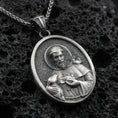Load image into Gallery viewer, Oxidized sterling silver Saint Francis pendant on textured volcanic rock, oval medallion with halo relief and bird detail, macro studio shot