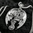 Load image into Gallery viewer, Polished silver dragon cross necklace pendant on dark volcanic stone, crisp wing edges and engraved cross pattern, premium close-up composition
