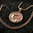 Load image into Gallery viewer, Rose gold plated Mortal Kombat dragon medallion on porous volcanic stone surface, raised dragon head emblem with textured field, sharp focus