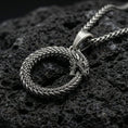 Load image into Gallery viewer, Oxidized ouroboros serpent pendant necklace photographed on volcanic rock with detailed ancient mythology scale texture
