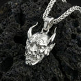 Load image into Gallery viewer, Polished silver Japanese oni mask pendant displayed on volcanic stone background with carved samurai spirit features