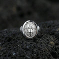 Load image into Gallery viewer, Polished silver wolf signet ring on volcanic rock, oval bezel framing a raised wolf portrait with sharp edge rim, premium close-up shot