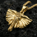 Load image into Gallery viewer, Gold plated elephant charm pendant displayed on porous volcanic rock surface, close-up studio composition, sharp tusk and trunk detailing