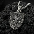 Load image into Gallery viewer, Oxidized Archangel Michael shield pendant on textured volcanic rock, macro close-up, detailed wings and sword relief, premium studio lighting