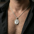 Load image into Gallery viewer, Polished silver Saint Andrew oval medallion pendant worn on chain, lifestyle framing, apostle figure and cross engraving visible