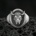 Load image into Gallery viewer, Oxidized sterling silver bull signet ring on textured volcanic rock, front-facing horned head relief with oval face in macro studio shot