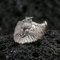 Load image into Gallery viewer, Polished silver owl ring on volcanic rock surface, close-up highlighting detailed feather texture, wide wingspan design, and clean metal contours