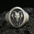 Load image into Gallery viewer, Oxidized sterling silver elephant signet ring on textured volcanic rock, macro close-up showing oval face with frontal elephant head, tusks, and trunk detail