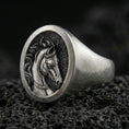 Load image into Gallery viewer, Oxidized sterling silver horse signet ring on textured volcanic rock, macro close-up showing round face with engraved stallion portrait and dark recessed background