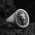 Load image into Gallery viewer, Oxidized sterling silver lion signet ring on textured volcanic rock, macro close-up highlighting the roaring lion head relief and dark recessed background