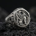 Load image into Gallery viewer, Detailed griffon ring crafted in oxidized sterling silver, winged mythical creature relief, macro product shot on textured volcanic rock background