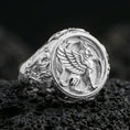Load image into Gallery viewer, Polished silver griffon ring featuring sculpted griffin body and feathered wings, centered close-up jewelry photo on dark porous volcanic stone