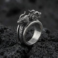 Load image into Gallery viewer, Detailed twin dragons ring crafted in oxidized sterling silver, two dragon heads meeting on an open band with scale texture, macro product shot on textured volcanic rock background
