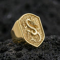 Load image into Gallery viewer, Gold plated Chinese dragon shield signet ring with high-relief dragon motif and textured background, premium studio macro on black porous volcanic rock surface