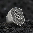Load image into Gallery viewer, Bold Chinese dragon shield signet ring crafted in oxidized sterling silver, raised coiled dragon relief on textured signet face, macro product shot on volcanic rock background