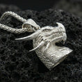 Load image into Gallery viewer, Polished silver dragon head pendant on dark volcanic stone, sharp fang and scale relief, premium close-up composition