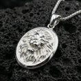 Load image into Gallery viewer, Polished silver lion head oval pendant necklace on dark volcanic stone, crisp mane detail and smooth bezel edge, premium close-up composition