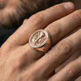 Load image into Gallery viewer, Rose gold plated Eucharist signet ring worn on finger, oval Eucharist signet face with chalice and host engraving, cross band