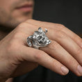 Load image into Gallery viewer, Polished silver horned skull ring on the finger, wearable shot highlighting sharp horn silhouette and detailed wood-grain carving