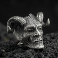 Load image into Gallery viewer, Oxidized sterling silver horned skull ring on black volcanic rock, macro close-up showing carved wood-grain texture and deep shadowed details