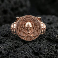 Load image into Gallery viewer, Rose gold plated Viking warrior ring on textured volcanic rock, luxury close-up capturing warm tone, intricate knotwork frame and skull helmet centerpiece