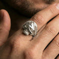 Load image into Gallery viewer, Polished silver Roman laurel skull ring on the finger, wearable shot highlighting sculpted leaf wreath and the skull’s hollow eyes