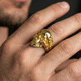 Load image into Gallery viewer, Gold plated skull biker ring worn on a finger, lifestyle photo emphasizing bold warm plating tone, claw hand grip design and heavy metal aesthetic