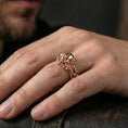Load image into Gallery viewer, Gold plated skull ring with vine wrap worn on a finger, lifestyle image emphasizing warm plating tone, intricate gothic sculpting and edgy biker style