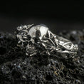 Load image into Gallery viewer, Polished silver skull and vine ring on porous volcanic stone, close-up highlighting bright shine, sharp skull detail and intertwined chain-like branches
