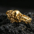 Load image into Gallery viewer, Gold plated skull ring with thorn vine band on volcanic rock, premium macro photo showcasing warm tone, high-relief gothic carving and rugged texture