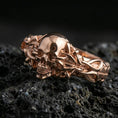 Load image into Gallery viewer, Rose gold plated skull with twisted vine ring on textured volcanic rock, luxury close-up capturing warm plating glow and detailed gothic skull sculpting